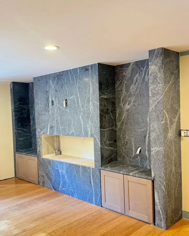 A full wall in dark veined stone around a fireplace niche and built-in cabinets