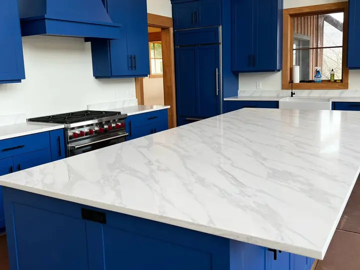 White marble-look island and counters set against navy blue cabinets and a navy range hood