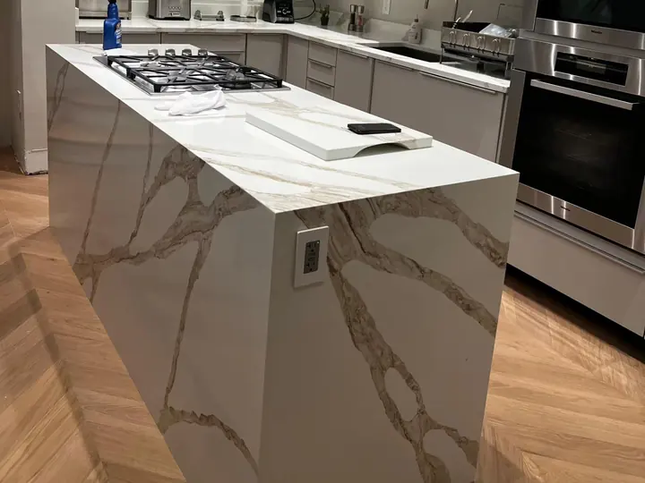 Kitchen island with waterfall ends in white quartz with gray and gold veins, a cooktop on top
